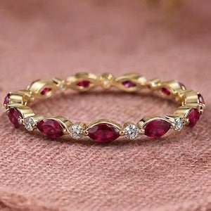Könnte beinhalten: Ein Goldring als Ewigkeitsband mit einem abwechselnden Muster aus marquise-geschliffenen roten Rubinen und kleinen runden weißen Diamanten. Der Ring besteht aus einem dünnen Metallband, das jeden Edelstein in einer sicheren Fassung hält.