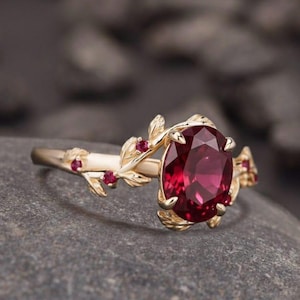 May include: A gold ring with a large oval ruby gemstone and small red accent stones. The ring features a leaf and vine design. The text "foreverjewellstudio" is at the top of the image.