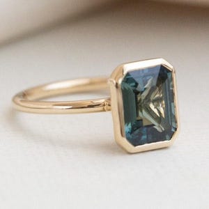 May include: A gold ring featuring a large, emerald-cut blue gemstone. The ring is set on a plain band.