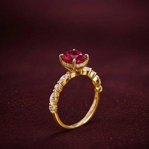K&ouml;nnte beinhalten: Ein goldener Ring mit einem gro&szlig;en, runden, roten Edelstein als Mittelpunkt. Der Ring hat kleinere, klare Edelsteine und ein detailliertes Band. Der Hintergrund ist ein tiefes Burgunderrot, das das Design des Rings hervorhebt.