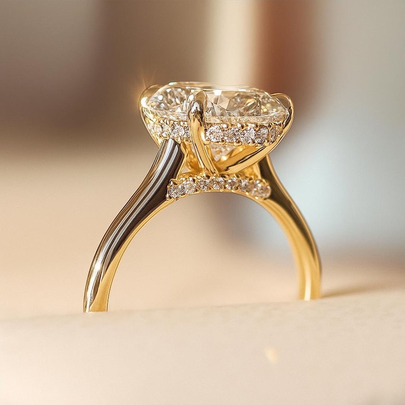 Puede incluir: Un anillo de compromiso de oro con un diamante grande y claro de talla ovalada como pieza central. El anillo presenta un halo de diamantes m&aacute;s peque&ntilde;os alrededor de la piedra principal y a lo largo de la banda, creando un efecto brillante. La banda es de oro pulido.