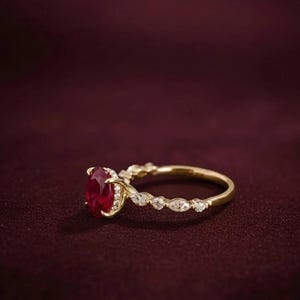 K&ouml;nnte beinhalten: Ein goldener Ring mit einem gro&szlig;en, oval geschliffenen Rubin als Mittelpunkt. Das Band weist kleine, klare Akzentsteine und ein filigranes Design auf. Der Ring ist vor einem dunkelroten Hintergrund platziert.