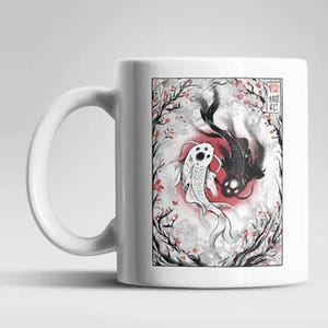 Könnte beinhalten: Ein weißer Keramikbecher mit einer rechteckigen Illustration von einem schwarzen und einem weißen Koi-Karpfen, die kreisförmig vor einem roten Sonnenhintergrund schwimmen. Das Design zeigt schwarze Äste mit kleinen rosa Blüten und japanischen Schriftzeichen.