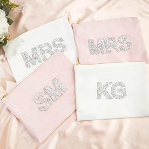 May include: Four white and pink zippered pouches with the words "MRS", "SM", "KG", and "MRS" in silver glitter.