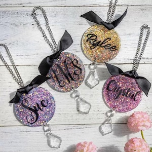 May include: Four car air fresheners with glitter and crystal charms. The charms are hanging from silver chains. The air fresheners are decorated with black ribbon bows and have personalized names: "Sue", "MMS", "Crystal", and "Rylee".