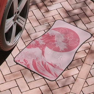 May include: A pink car floor mat featuring a Japanese wave design and the word "日本" (Japan) in white. The mat also includes the word "Drivade" in white.