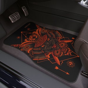 May include: Black car floor mat with an orange and black illustration of a cat wearing a samurai helmet. The illustration is surrounded by geometric shapes and arrows.