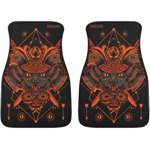 May include: A pair of black car floor mats with an orange samurai cat design. The design features a cat wearing a samurai helmet with swords and a geometric pattern.