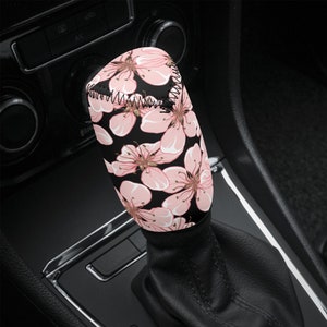 May include: A pink and black floral patterned gear shift knob cover. The cover is made of a soft, comfortable material and is designed to fit most standard gear shift knobs.