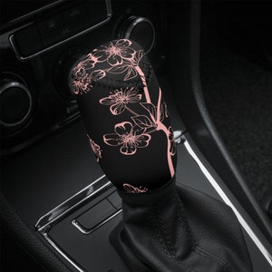 May include: Black gear stick knob cover with a pink floral design. The cover is made of a soft, comfortable material and fits over the existing gear stick knob.