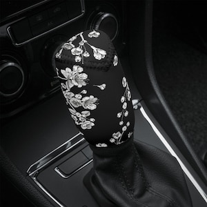 以下が含まれることがあります： 白い花柄の黒いシフトノブカバー。