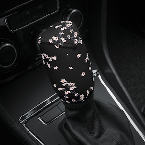 May include: Black gear stick knob cover with a white floral pattern. The cover is made of a soft, comfortable material and is designed to protect and enhance the look of your gear stick knob.
