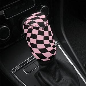 May include: A pink and black checkered gear shift knob cover. The cover is made of a soft, comfortable material and is designed to fit most standard gear shift knobs.
