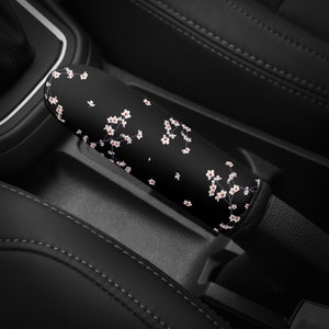 May include: Black car gear shift knob cover with a white floral pattern.