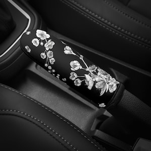 May include: Black car gear shift knob cover with a white floral design.