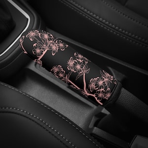 May include: Black car gear shift cover with a pink floral design.