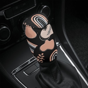 May include: A black gear shift knob cover with a colorful abstract pattern featuring rainbows, leaves, and peach-colored shapes.