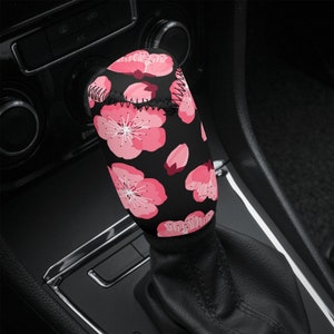 May include: A black gear stick knob cover with a pink floral pattern. The cover is made of a soft, comfortable material and is designed to protect the gear stick knob from wear and tear.
