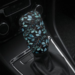May include: A black gear stick knob with a blue and green floral pattern. The gear stick knob is in a car.