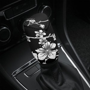 May include: Black and white floral patterned gear shift knob cover. The cover is made of a soft, flexible material and fits over the gear shift knob.