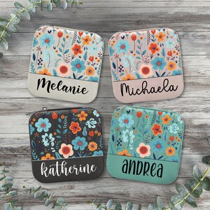 May include: Four zippered pouches with floral patterns and personalised names. The pouches are in shades of pink, beige, black, and teal. The names are Melanie, Michaela, Katherine, and Andrea.