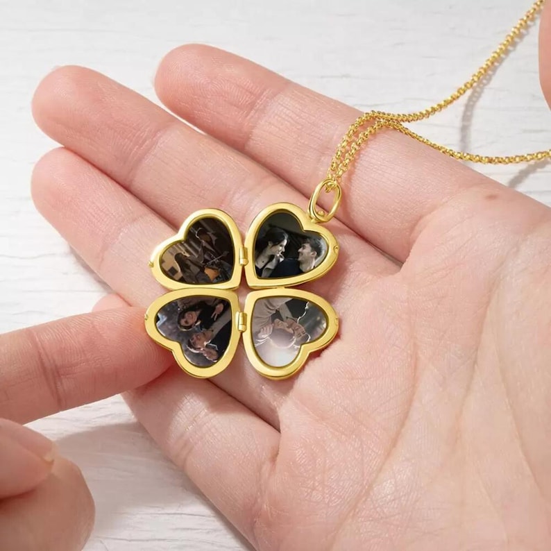 May include: Gold necklace with a four-leaf clover locket that opens to reveal four photo slots. Each slot has a different photo of people.