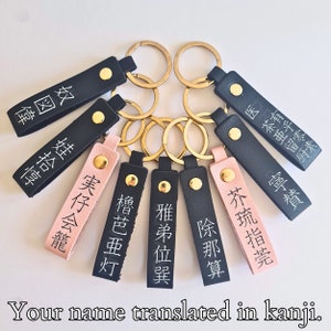 May include: A set of ten keychains with black and pink leather straps. Each keychain has a gold metal ring and a black or pink leather tag with Japanese characters. The text on the tags reads: "医茶亜留厨", "有乎零素", "奴図偉", "寧賛", "芥琉指莞", "除那算", "雅弟位巽", "●櫓芭亜灯", "●実仔会籠", and "娃拾惇".