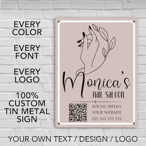 May include: A pink and white metal sign with a black outline of a hand with leaves around it. The text "Monica's nail saloon" is written in black cursive font. A QR code is in the bottom left corner. The text "SOCIAL MEDIA YOUR WEBSITE 555 111 222 333" is written in black font. The text "YOUR OWN TEXT / DESIGN / LOGO" is written in black font at the bottom of the sign.
