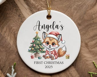 Può includere: Ornamento natalizio rotondo in ceramica bianca con cordino dorato. Presenta una volpe dei cartoni animati con cappello da Babbo Natale e abito rosso, un albero di Natale e la scritta "Angela's First Christmas 2025".