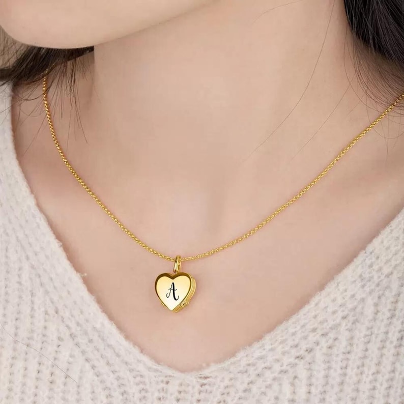 May include: A gold chain necklace with a heart-shaped pendant. The pendant has the letter "A" engraved on it.