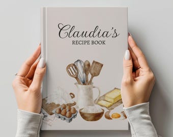 Puede incluir: Un libro de recetas blanco con el título "Claudia's Recipe Book" en letra cursiva negra. La portada presenta una ilustración de acuarela de utensilios de cocina, harina, huevos y mantequilla.