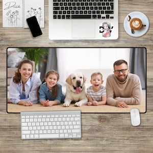 Op de afbeelding: Een gezin van vier, inclusief een hond, ligt op een wit tapijt. Het gezin glimlacht en kijkt naar de camera. De hond is een witte Labrador Retriever. Het gezin is in een woonkamer met een witte muur en een houten vloer.