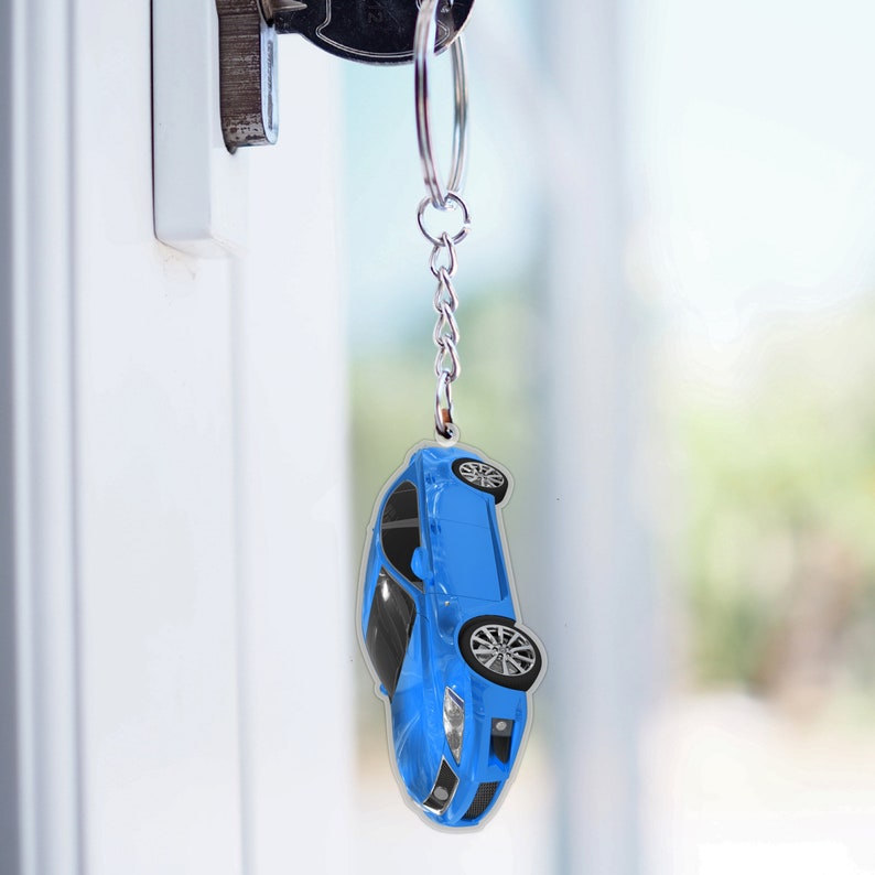 May include: A blue car keychain with a silver key ring. The car is facing downwards and has a black interior.