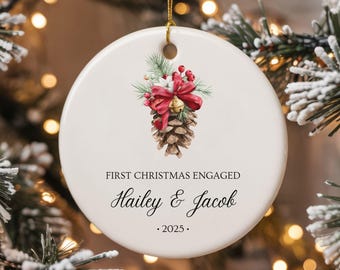 Puede incluir: Un adorno navideño de cerámica blanca con una piña, un lazo rojo y una campana. El adorno dice "First Christmas Engaged Hailey & Jacob . 2025."