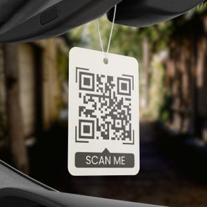 May include: White car air freshener with a black and white QR code and the text "SCAN ME" printed on it.