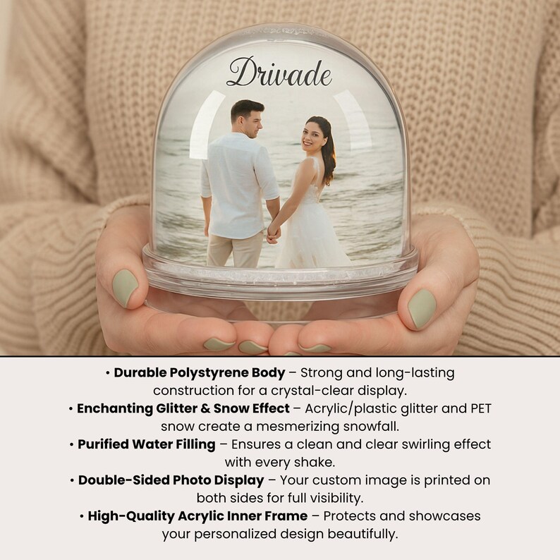 Może przedstawiać: Przezroczysta kula śnieżna ze zdjęciem pary trzymającej się za ręce na plaży. Na g&oacute;rze napis "Drivade" w ozdobnej czcionce. Kulę trzyma osoba.