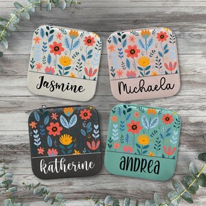 May include: Four zippered pouches with floral patterns and personalised names. The pouches are in beige, pink, black, and teal.