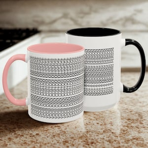 May include: Two white ceramic mugs with black and white geometric patterns. One mug has a pink interior and handle, the other has a black interior and handle. The mugs are on a speckled countertop.