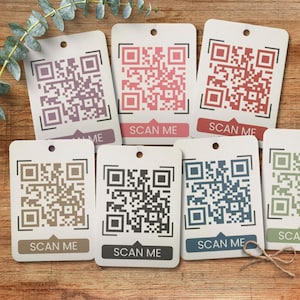 Puede incluir: Ocho tarjetas cuadradas blancas con bordes negros y códigos QR en diferentes colores. Cada tarjeta tiene el texto "SCAN ME" impreso.
