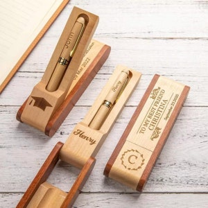 Puede incluir: Tres portaplumas de madera con grabados personalizados. El primer portaplumas tiene un gorro de graduación y el nombre "John" grabado en él. El segundo portaplumas tiene el nombre "Henry" grabado en él. El tercer portaplumas tiene el texto "To my best friend Christina" y una letra "C" en una corona grabada en él.