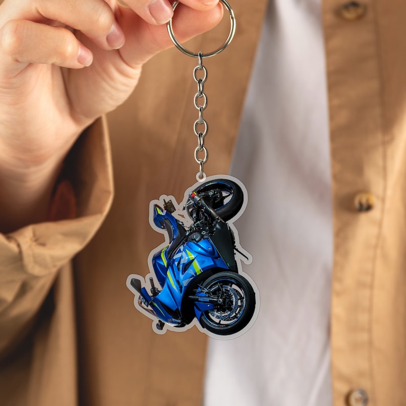 May include: A blue and white motorcycle keychain with a silver key ring. The motorcycle is in a wheelie position.