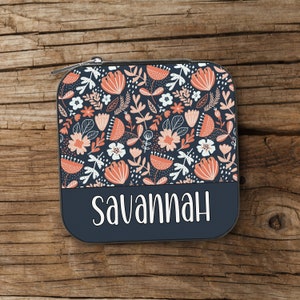May include: A dark blue zippered pouch with a floral pattern in shades of pink and white. The pouch has a personalised name, "Savannah", printed in white on the bottom.