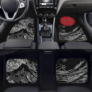 May include: Black car floor mats featuring a white wave and mountain design. The mats are in the front and back of the car. One mat has a red circle with Japanese text.