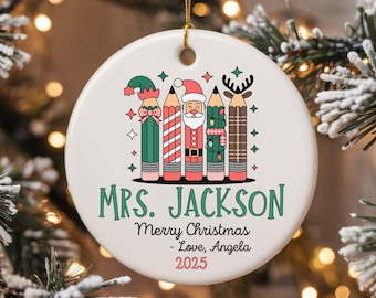 May include: A white ceramic Christmas ornament with a gold string. The ornament features a pencil design with Santa, reindeer, and elf hats. Text reads "MRS. JACKSON Merry Christmas - Love, Angela 2025."