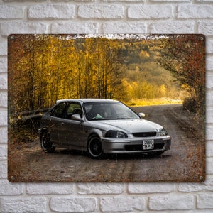 May include: A silver Honda Civic hatchback driving on a dirt road through a forest with yellow autumn leaves. The car has a license plate that reads "2580 BP-7".