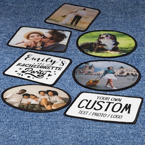May include: A set of nine iron-on patches with various designs. The patches are white with black outlines and feature images of people, animals, and text. The patches are on a blue denim background.