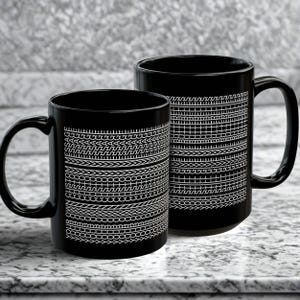Peut inclure: Deux mugs noirs en céramique avec des motifs géométriques blancs. Les mugs ont une finition brillante et une anse incurvée. Les motifs comprennent des lignes, des chevrons et des motifs en forme de chaîne. Les mugs sont posés sur une surface en marbre.