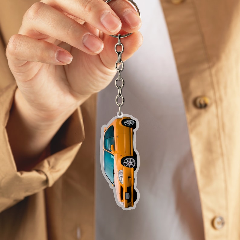 May include: A yellow car keychain with a silver chain. The car is facing upwards and has a black interior.