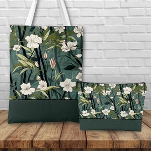 May include: A green tote bag and matching makeup bag with a white floral pattern. The pattern features white flowers and green leaves on a dark green background.