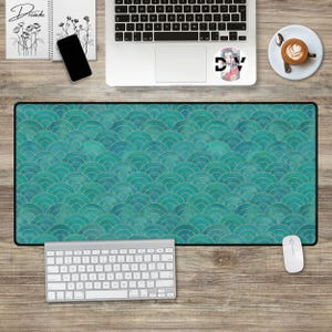 May include: A teal blue and gold desk mat with a repeating pattern of overlapping semi-circles. The mat is on a wooden desk with a laptop, keyboard, mouse, and a cup of coffee.
